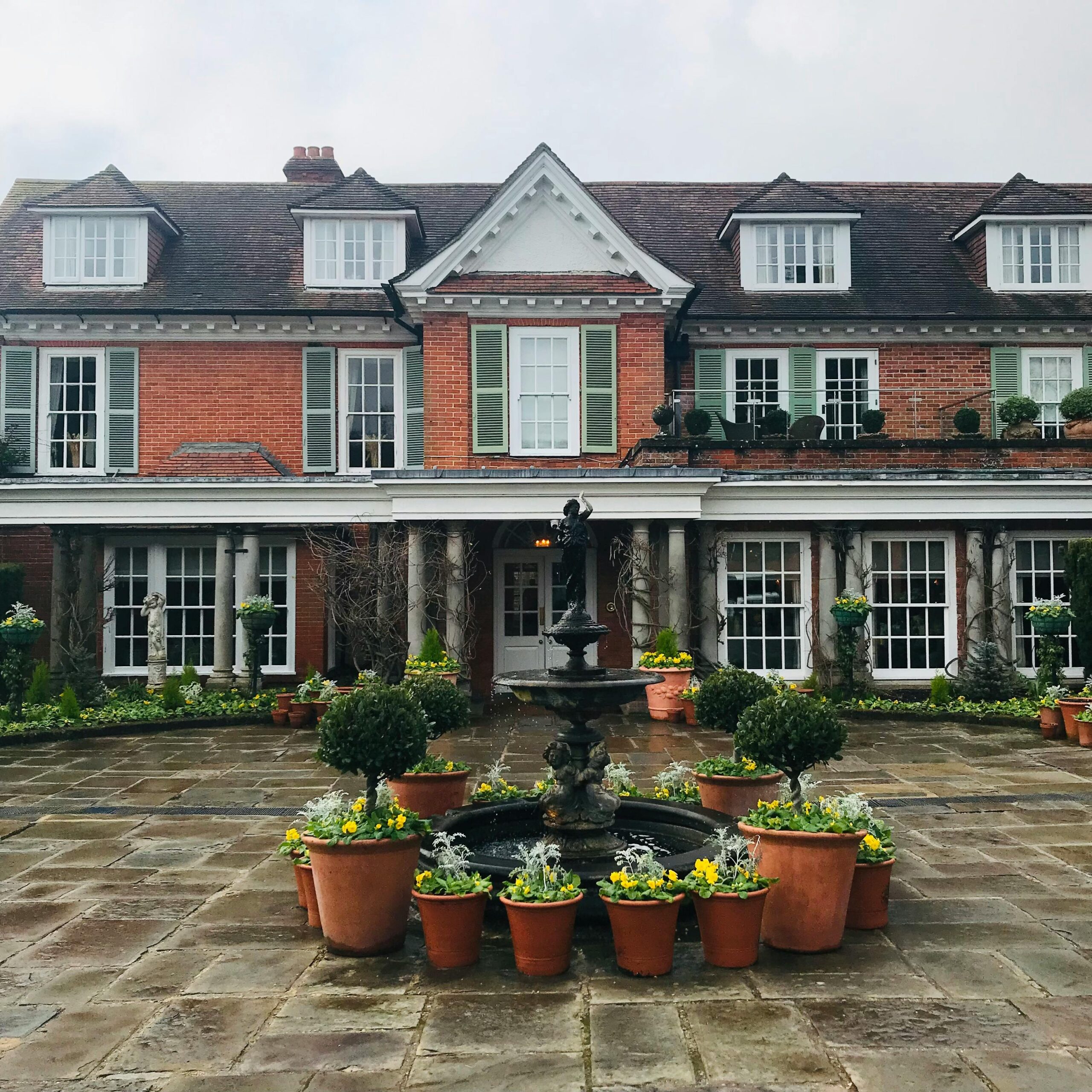 Charming brick house facade with a classic fountain and potted plants in the courtyard.