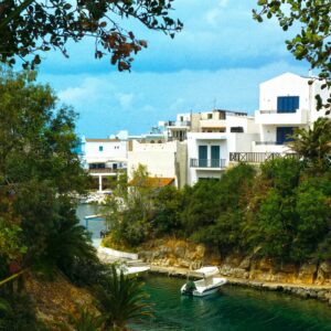 Picturesque scenery of turquoise water flowing along greenery shore with residential buildings in coastal city against blue sky in nature